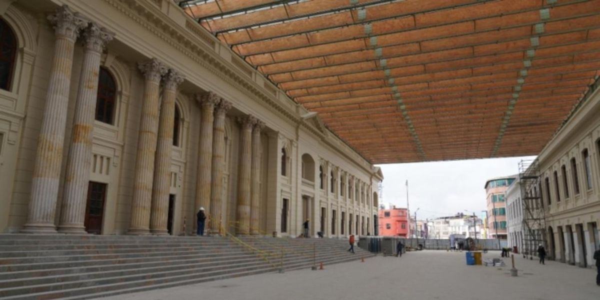 Edificio con columnas y amplias escalinatas bajo una cubierta. Varias personas están de pie o caminan en el patio central.