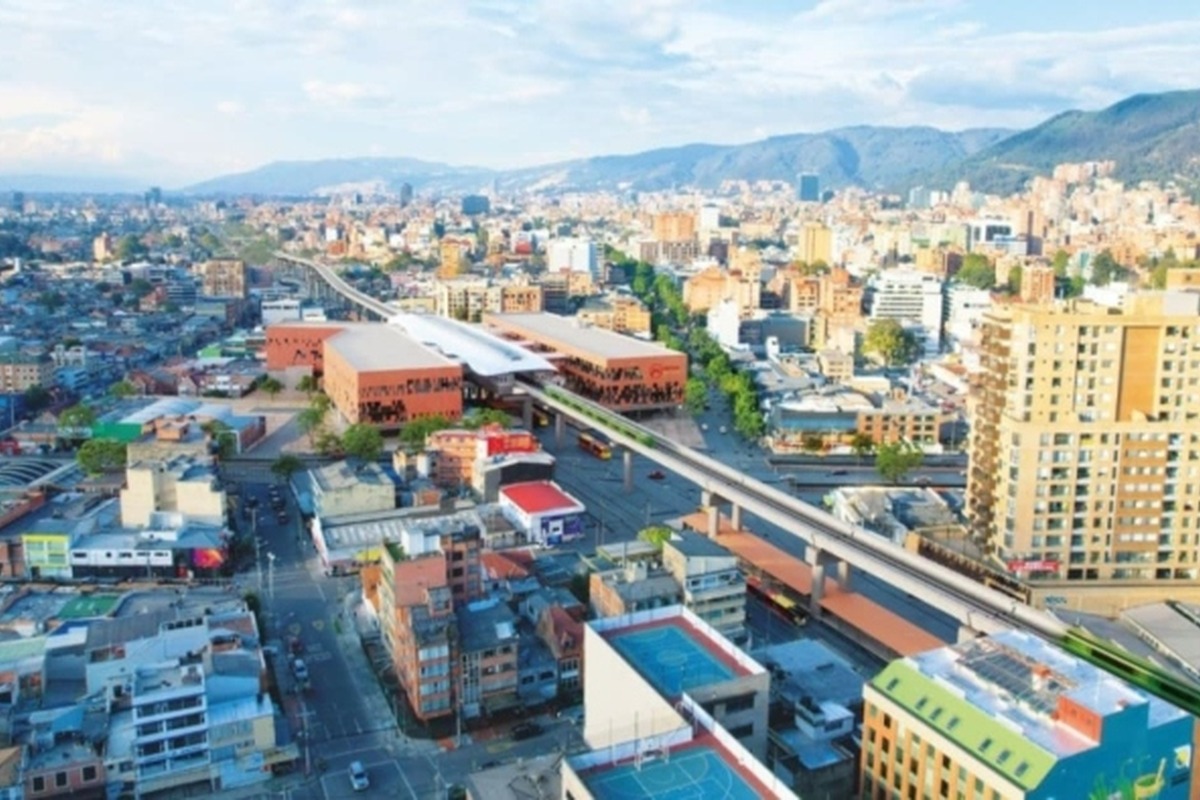 Vista aérea de ciudad con muchos edificios de distintos tamaños, montañas al fondo y un viaducto elevado que cruza el centro con estaciones y buses visibles debajo.
