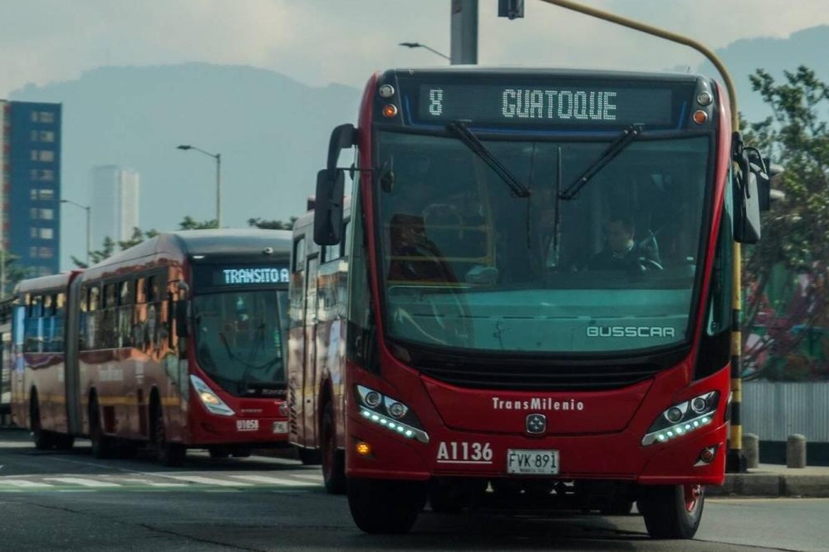 Dos buses rojos articulados de TransMilenio avanzan por una vía urbana
