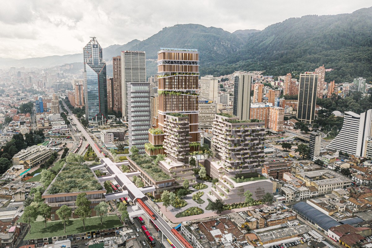 Vista aérea urbana con edificios altos, complejo con terrazas verdes, vía elevada con buses rojos y montañas al fondo.