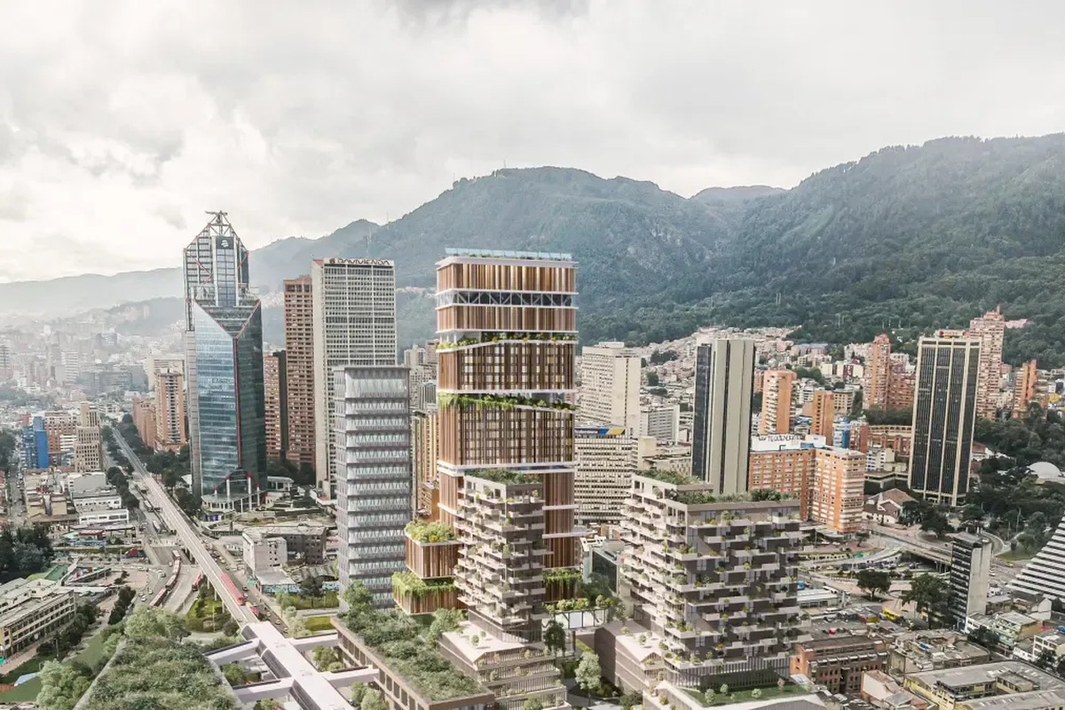 Vista aérea de ciudad con muchos rascacielos modernos, algunos con terrazas verdes. Al fondo se ven montañas boscosas y cielo nublado; abajo, avenidas con tráfico y edificios bajos.