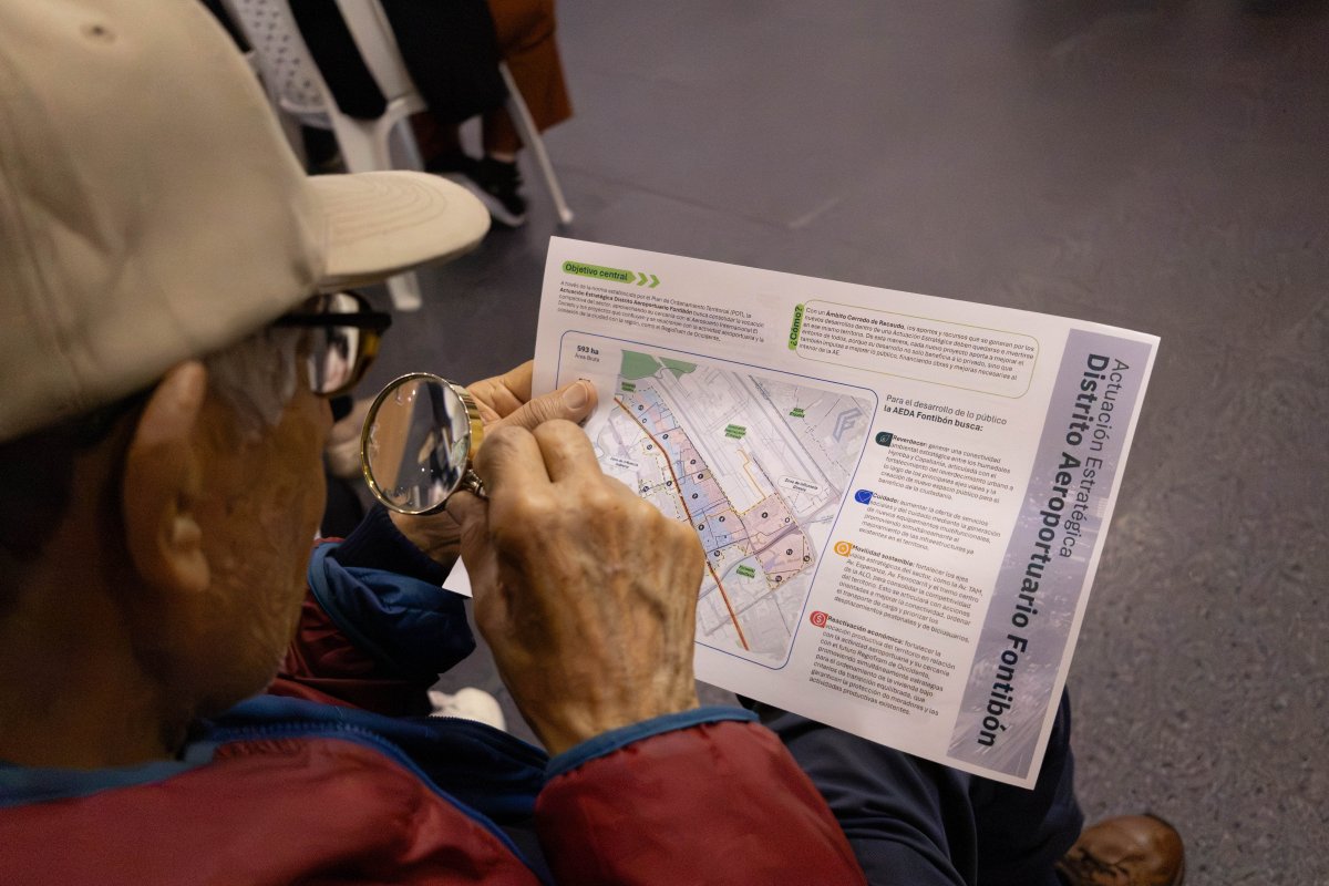 Persona sostiene un folleto con un mapa y lo observa con una lupa; lleva chaqueta roja y azul.