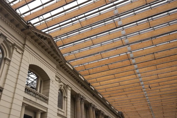 Interior de un edificio con fachada de estilo clásico, columnas y arcos, bajo una amplia cubierta de vidrio y estructura metálica.
